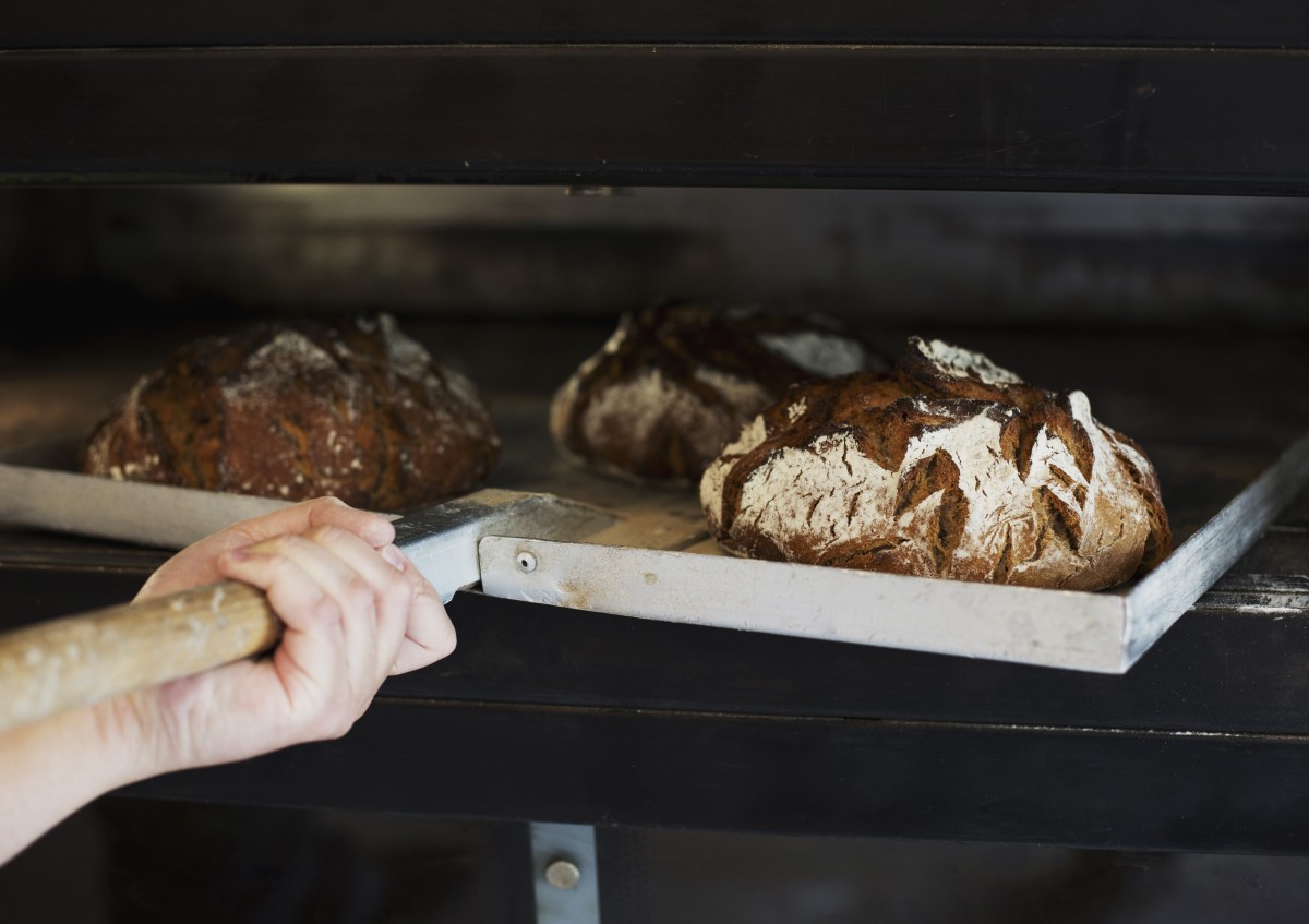 Das Foto zeigt wie mehrere Brote aus einem Ofen geholt werden.