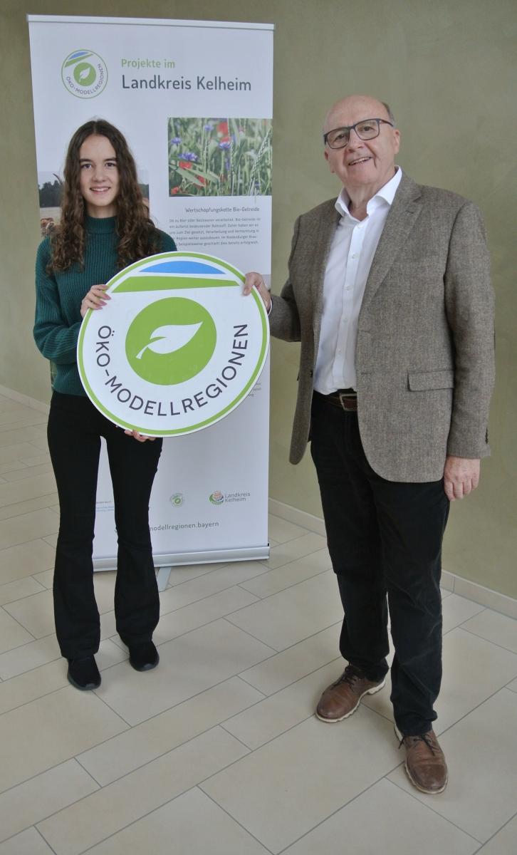 Zwei Personen halten ein Schild mit dem Logo der Öko-Modellregionen