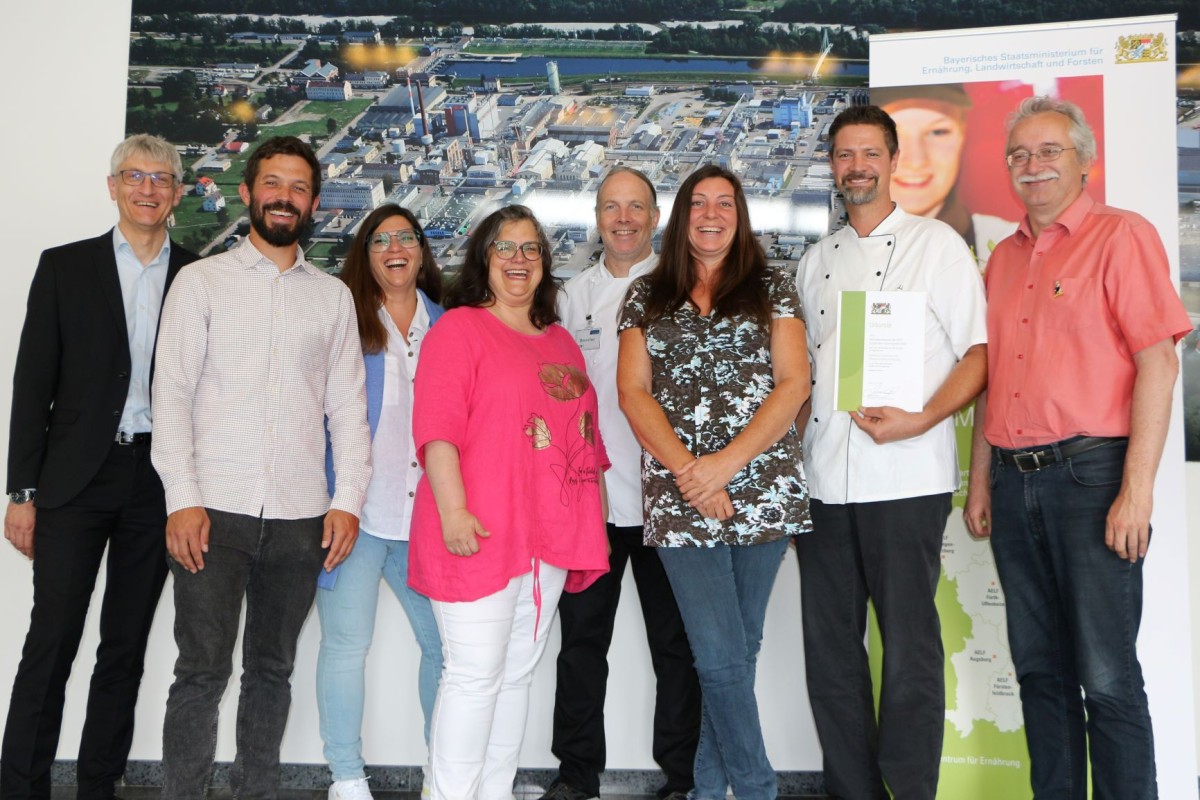 Das Foto zeigt eine Gruppe von Menschen, die vor einem  Plakat stehen. Eine Person hält eine Urkunde hoch.