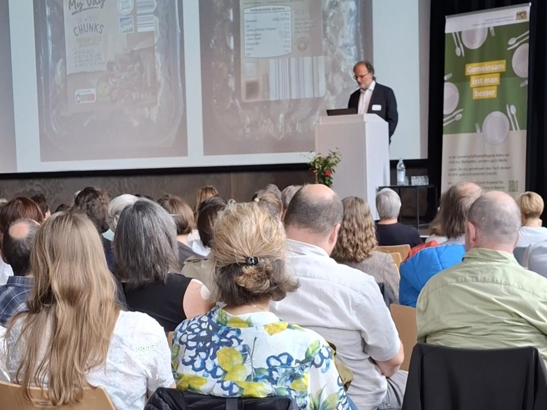 Menschen sitzen im Vortragssaal, einer spricht vorne.