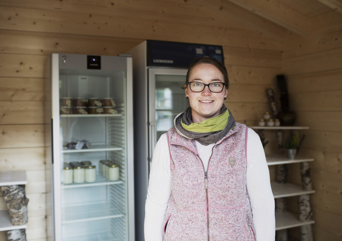 Eine Frau steht in einem Verkaufshaus aus Holz vor mehreren Kühlschränken.
