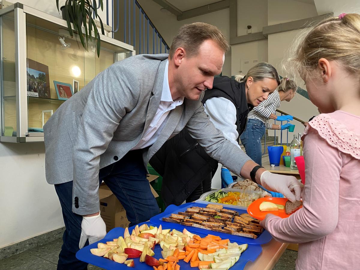 Drei Erwachsene vor einem gesunden Frühstücksbufett geben Kindern Essen aus