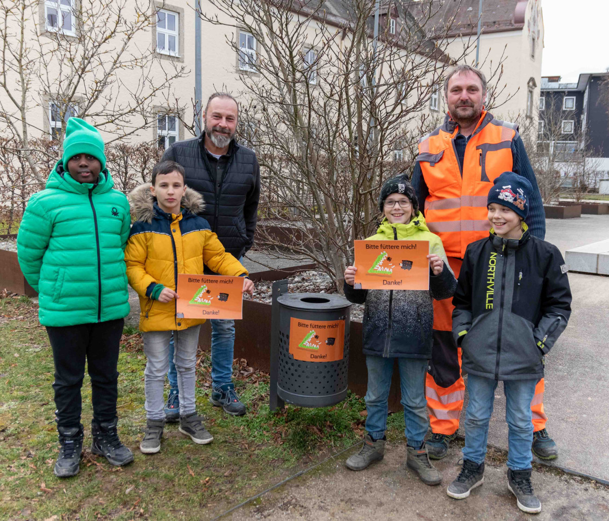 Peter Schweikl (l.), Leiter des Bauhofs, und Georg Schnaitl, stellvertretender Leiter des Bauhofs, mit (v.l.n.r.) Talla, Semin, Paul und David aus der 4b der Johannes-Hess-Schule vor dem ersten beklebten Mülleimer