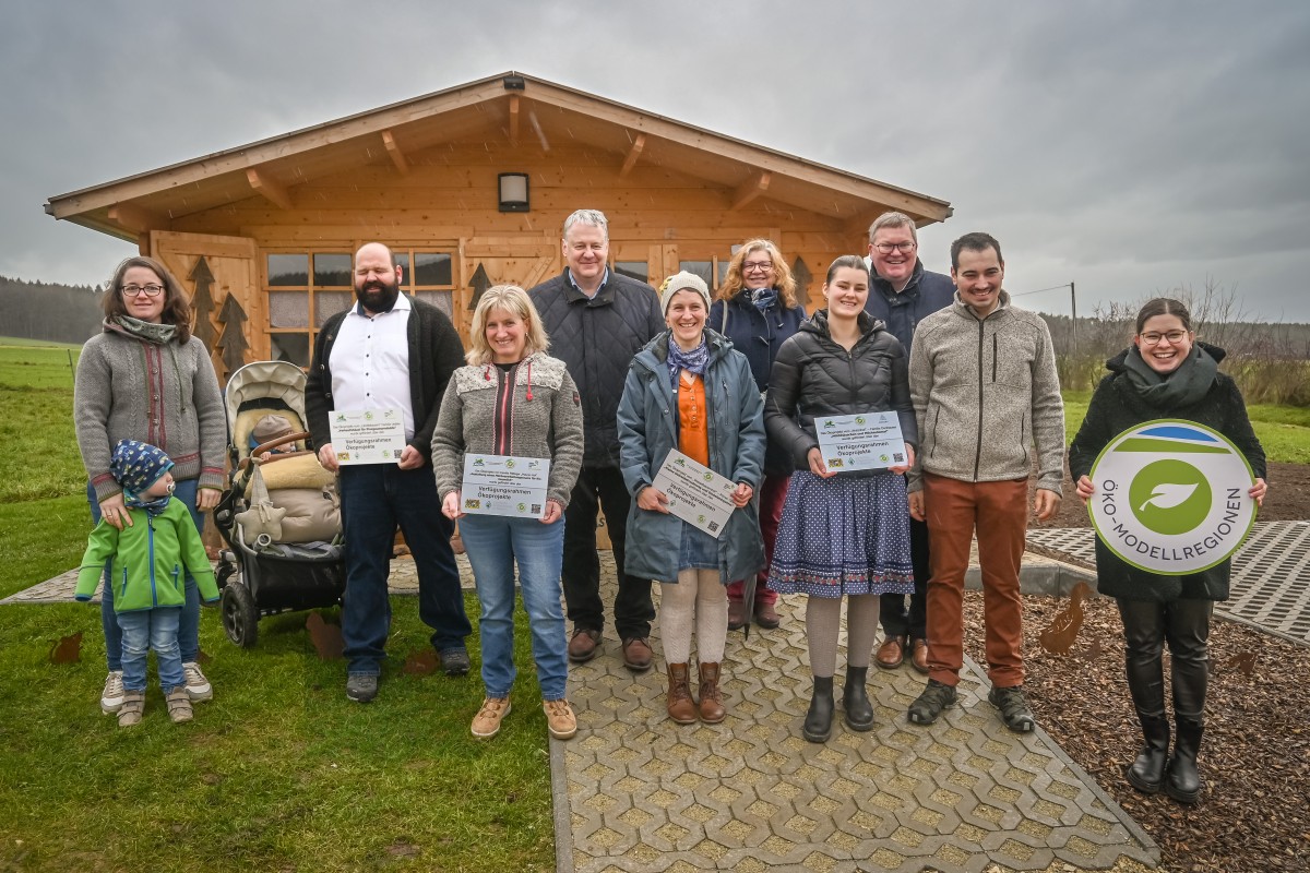 Mehrere Personen stehen vor einem Holzhäuschen und halten verschiedene Schilder in die Höhe.