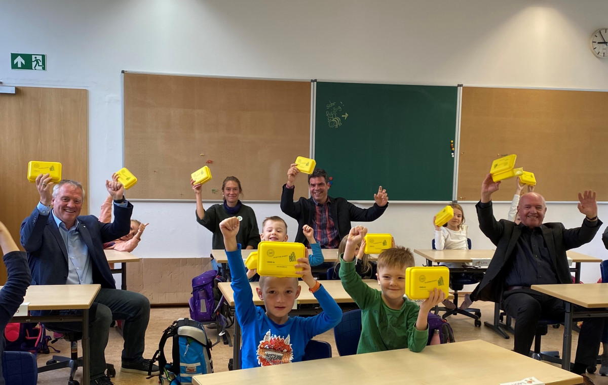 Landrat, Schulleitung und Kinder mit gelben Bio-Brotboxen im Klassenzimmer