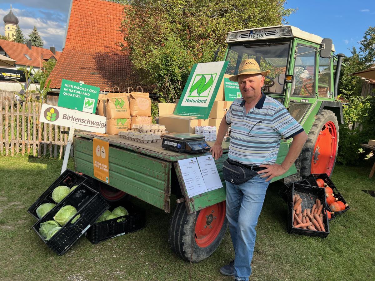 Ein Landwirt steht vor dem Traktor mit Waren vom Biohof: Eier, Gemüse und Kartoffeln