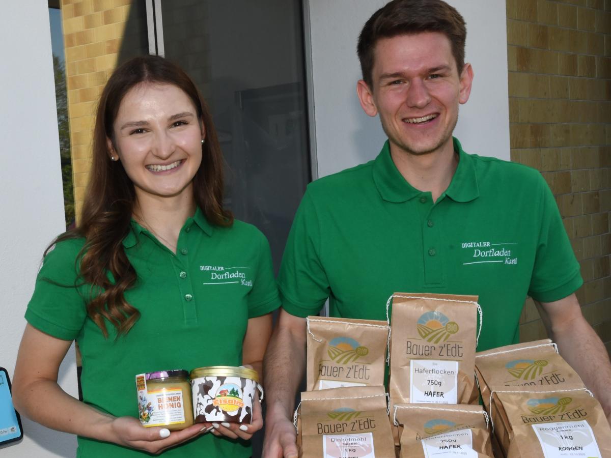 Zwei Personen mit grünen Poloshirts zeigen Produkte (Honig, Haferflocken)