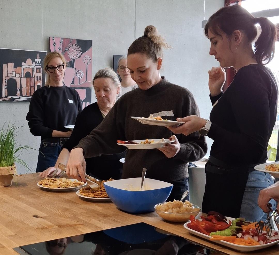 Mehrer Frauen bedienen sich am Buffett, z.B. Mörhenwaffeln und bunte Rohkost-Platte