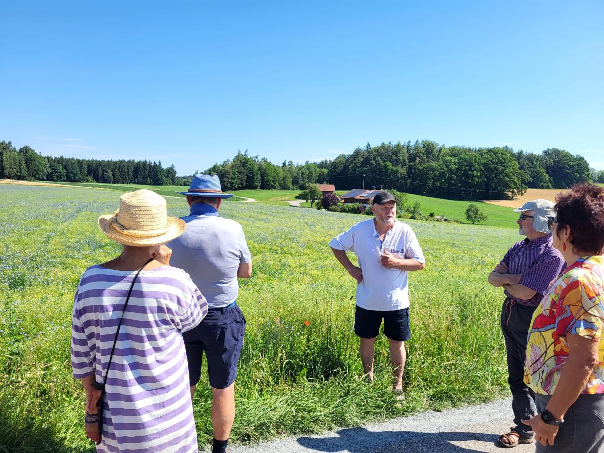 Die Teilnehmer der Exkursion hören Bio-Landwirt Franz Obermeyer aufmerksam zu, der ihnen direkt am Feld die Besonderheiten der beiden Saaten, Öl Lein und Leindotter, näherbringt.