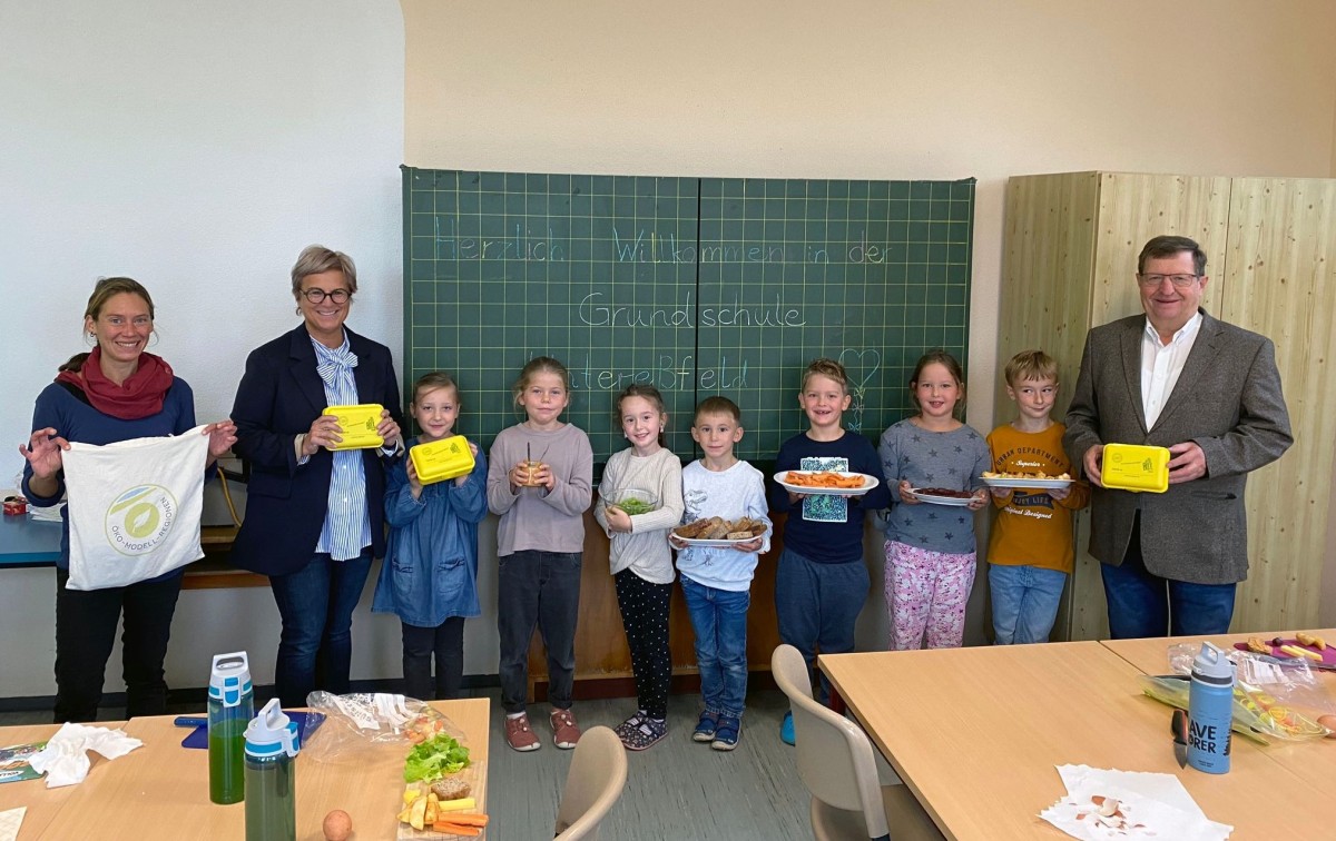 Personengruppe mit Frühstück und Brotboxen vor Tafel