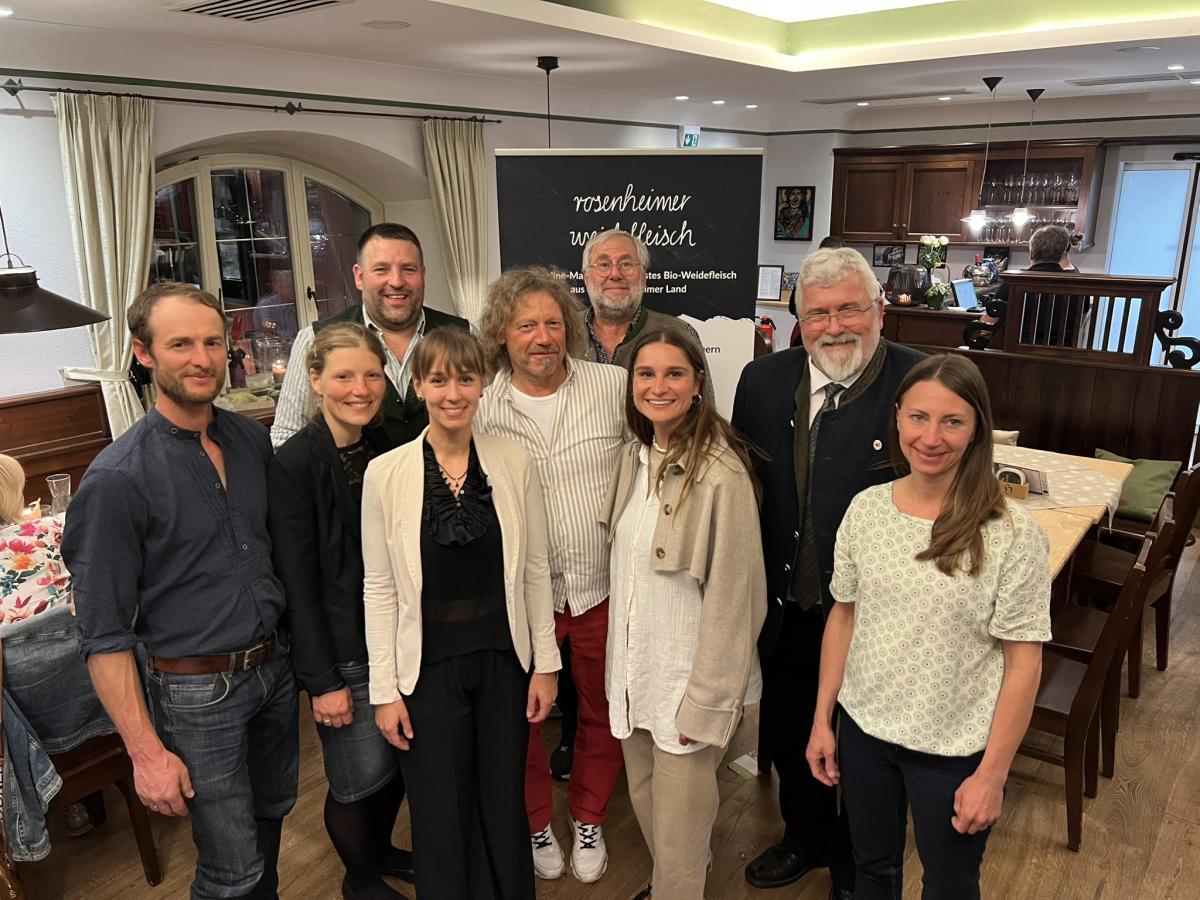 MdL Sebastian Friesinger mit Wirtin Veronika zur Hörst und den ÖMR-Managerinnen sowie mit Landwirtinnen und Landwirten von Rosenheimer Weidefleisch in einer Gaststube vor einem RollUp