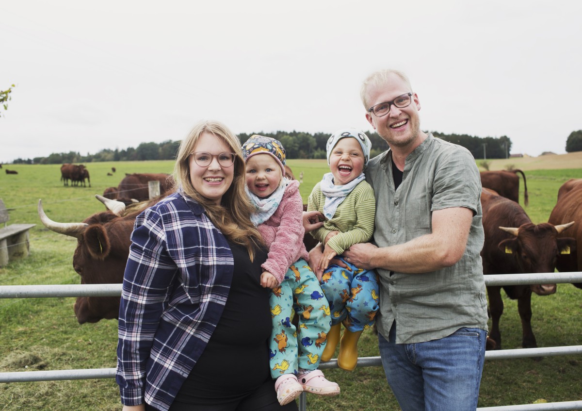 Zwei Erwachsene stehen mit zwei Kleinkindern vor einer Rinderherde.