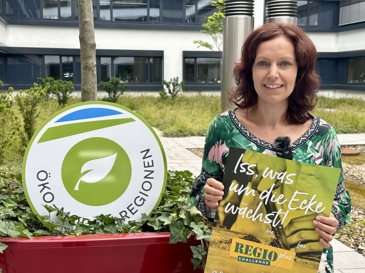 Projektleiterin Monika Ernst ruft mit Plakat zur Teilnahme an der Regioplus-Challenge auf