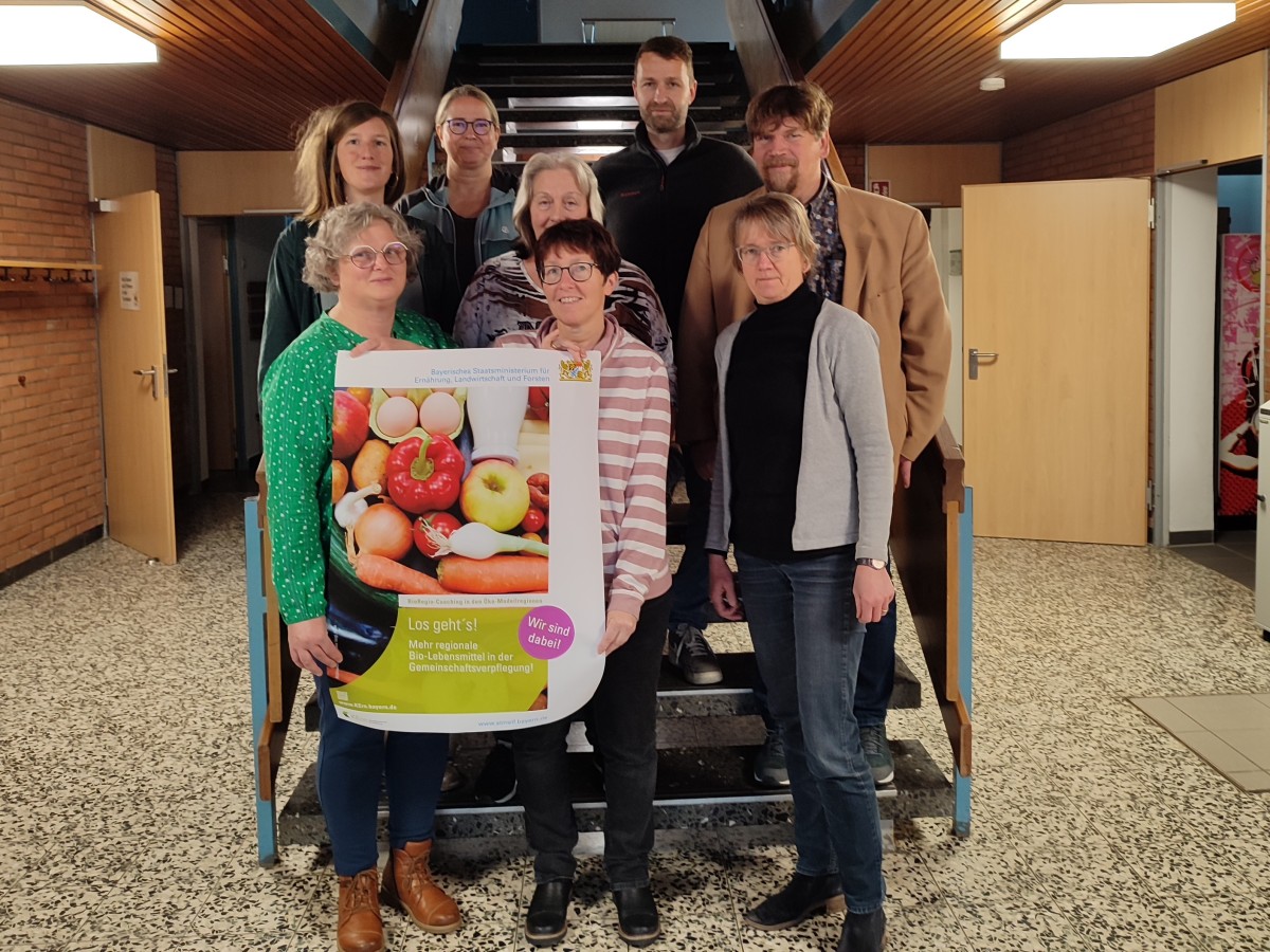 Acht Menschen in einem Treppenhaus mit dem Poster des BioRegioCoachings in der Hand