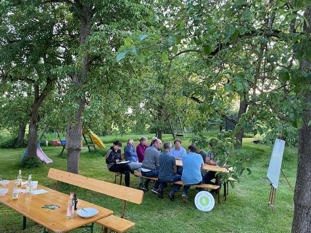 Menschen sitzen unter Bäumen an einer Bierzeltgarnitur