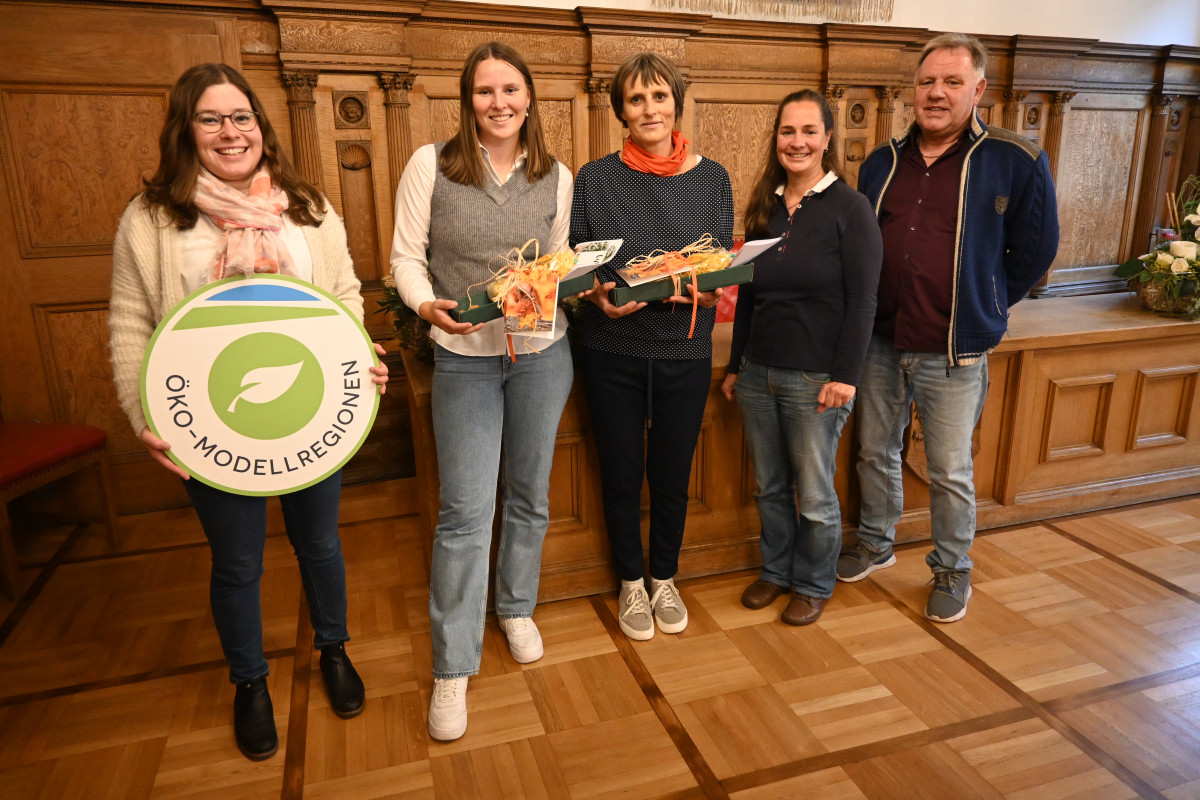 Fünf Personen stehen in einem Halbkreis vor einer holzbertäfelten Wand.