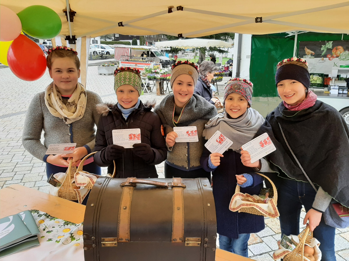 Fünf Apfelprinzessinnen in Trachtenjacken mit ausgefüllten Quizkarten stehen vor der Schatzkiste der Öko-Modellregion