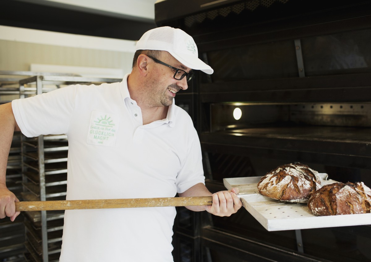 Das Foto zeigt einen Mann, der Brot in einen Ofen schiebt.