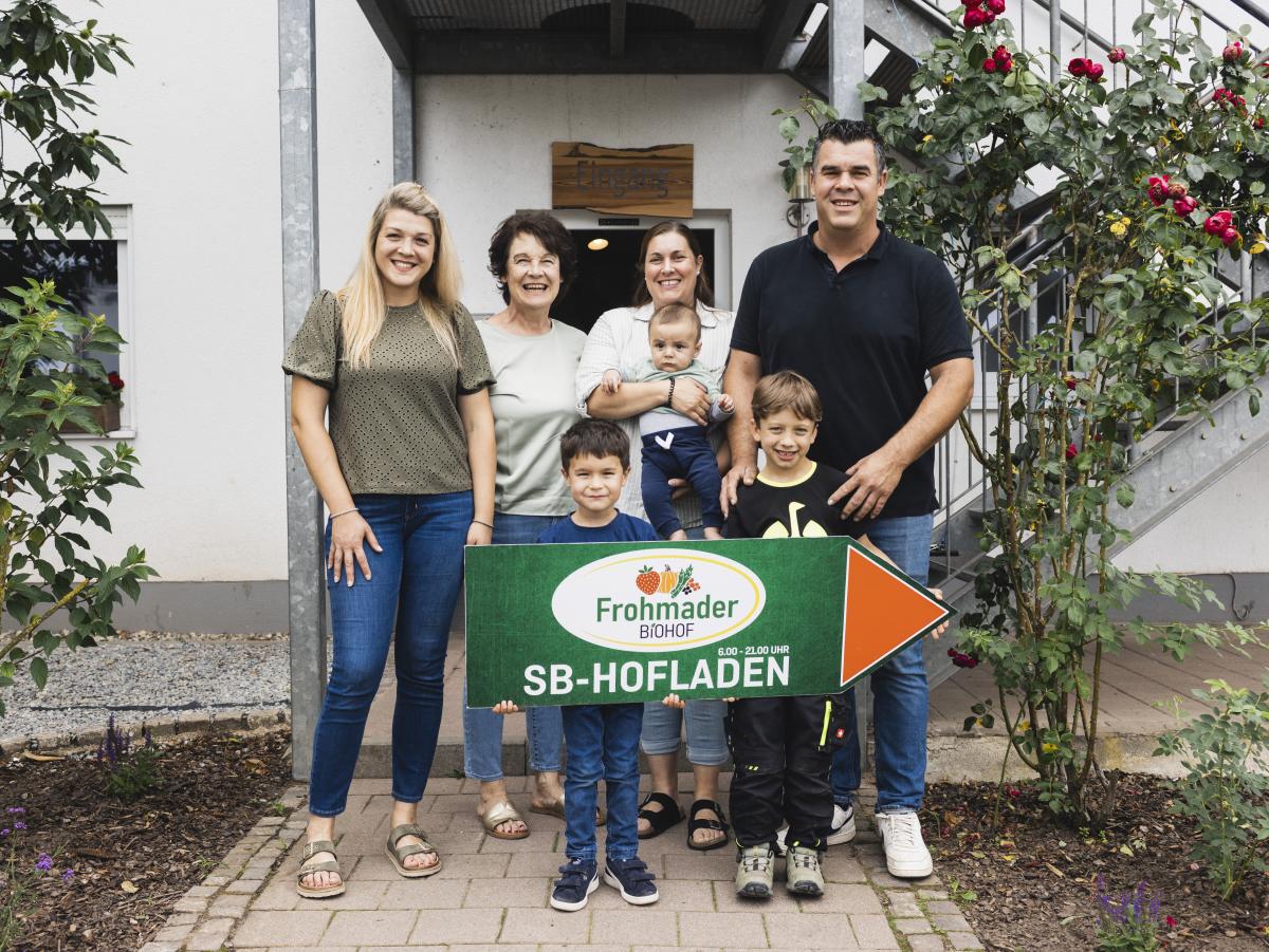 Vier Erwachsene und drei Kinder die das Hofschild vom Biohof Frohmader hochhalten