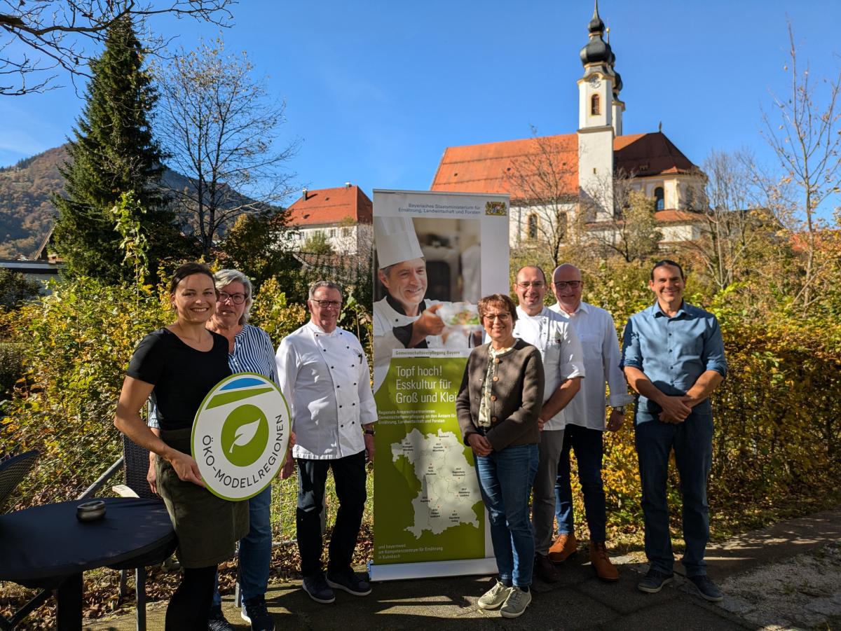 Eine Gruppe von Menschen steht im Freien, im Hintergrund die Aschauer Kirche