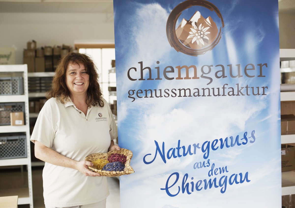 Geschäftsführerin Astrid Maier mit Ihren Produkten neben einem Rollup, dass die Chiemgauer Genussmanufaktur präsentiert