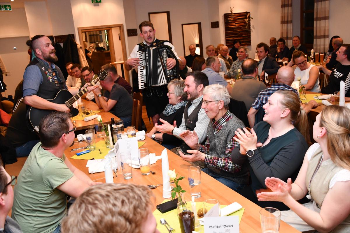 Gruppe von Menschen sitzt am Tisch und 2 Musiker spielen