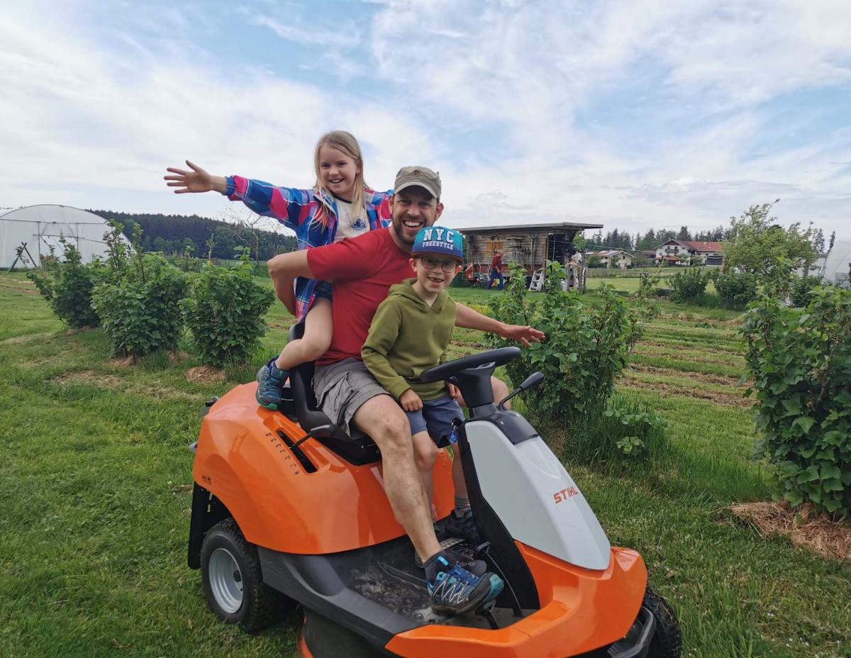 Ein Mann und Kinder sitzen auf einem Aufsitzrasenmäher.