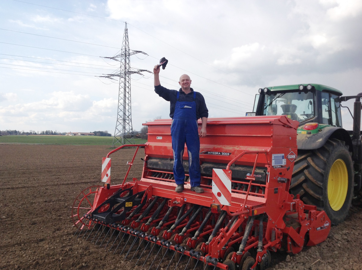 Wolfgang Aicher grüßend auf seiner  Sämaschine stehend in seinem Acker