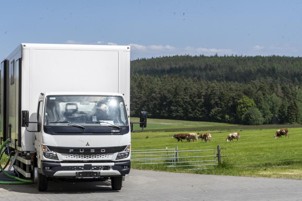 weißer LKW steht zwischen Stall und einer Kuhweide um die dortige Milch zu Käse zuverarbeiten