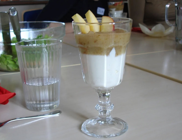 Glas mit Nachspeise: Naturjoghurt, Apfelkompott, Deko aus Apfelscheiben - daneben ein Glas Wasser