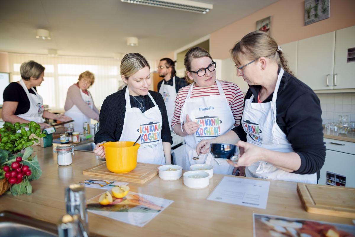 Mehrere Frauen - je mit weißer Schürze - bereiten Essen zu.