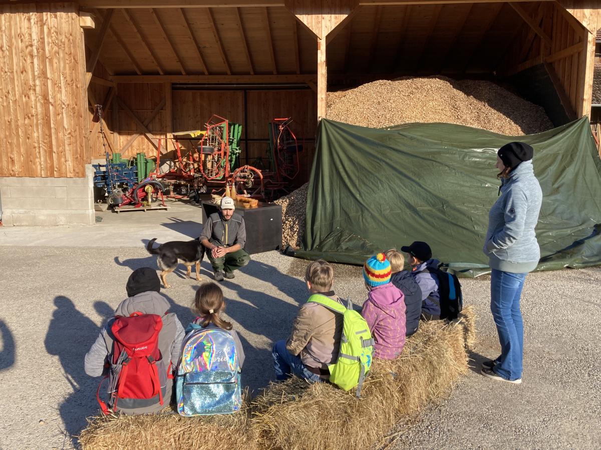 Kinder sitzen im Halbkreis um Mann herum und hören zu