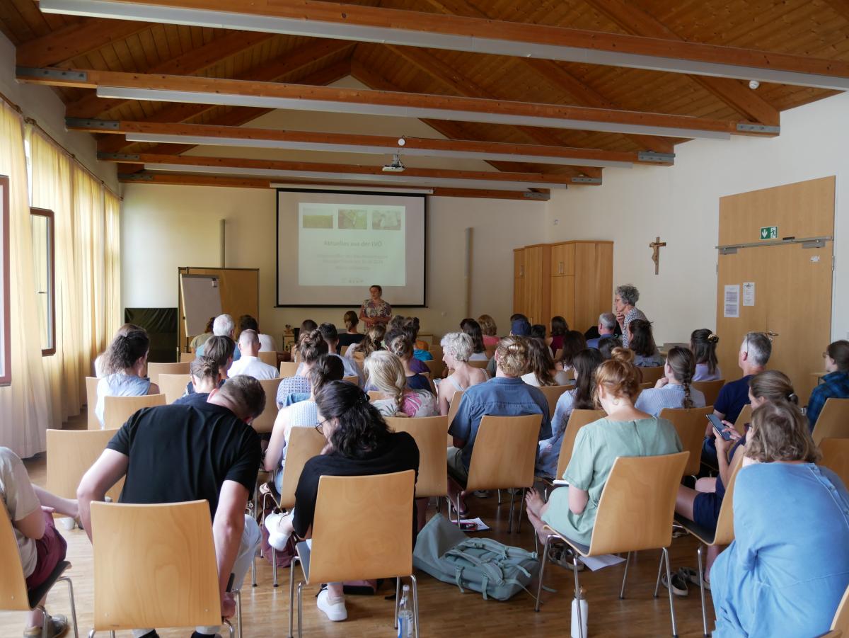 Menschen in auf Stühlen in einem Seminarraum vor einer Leinwand mit Präsentation