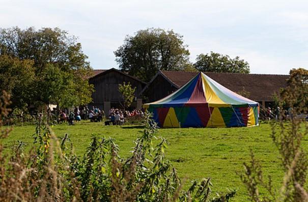 Buntes Zelt und feiernde Menschan am Hof im Sonnenschein.