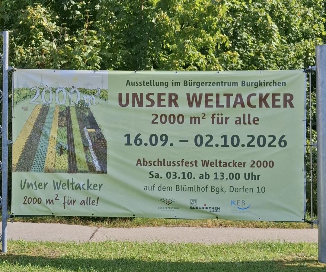 Banner mit den Ausstellungsterminen darauf im Freien bei Sonnenschein auf der Wiese mit Bäumen im Hintregrund.
