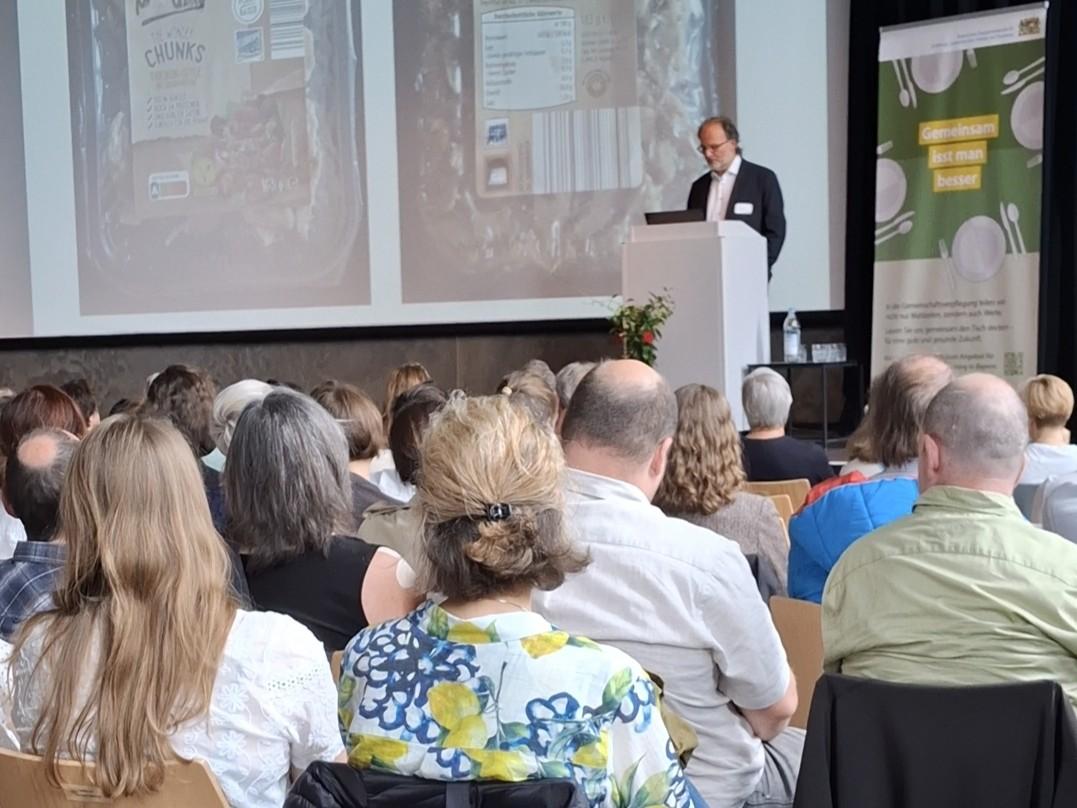 Einer spricht im Saal, viele hören sitzend zu.