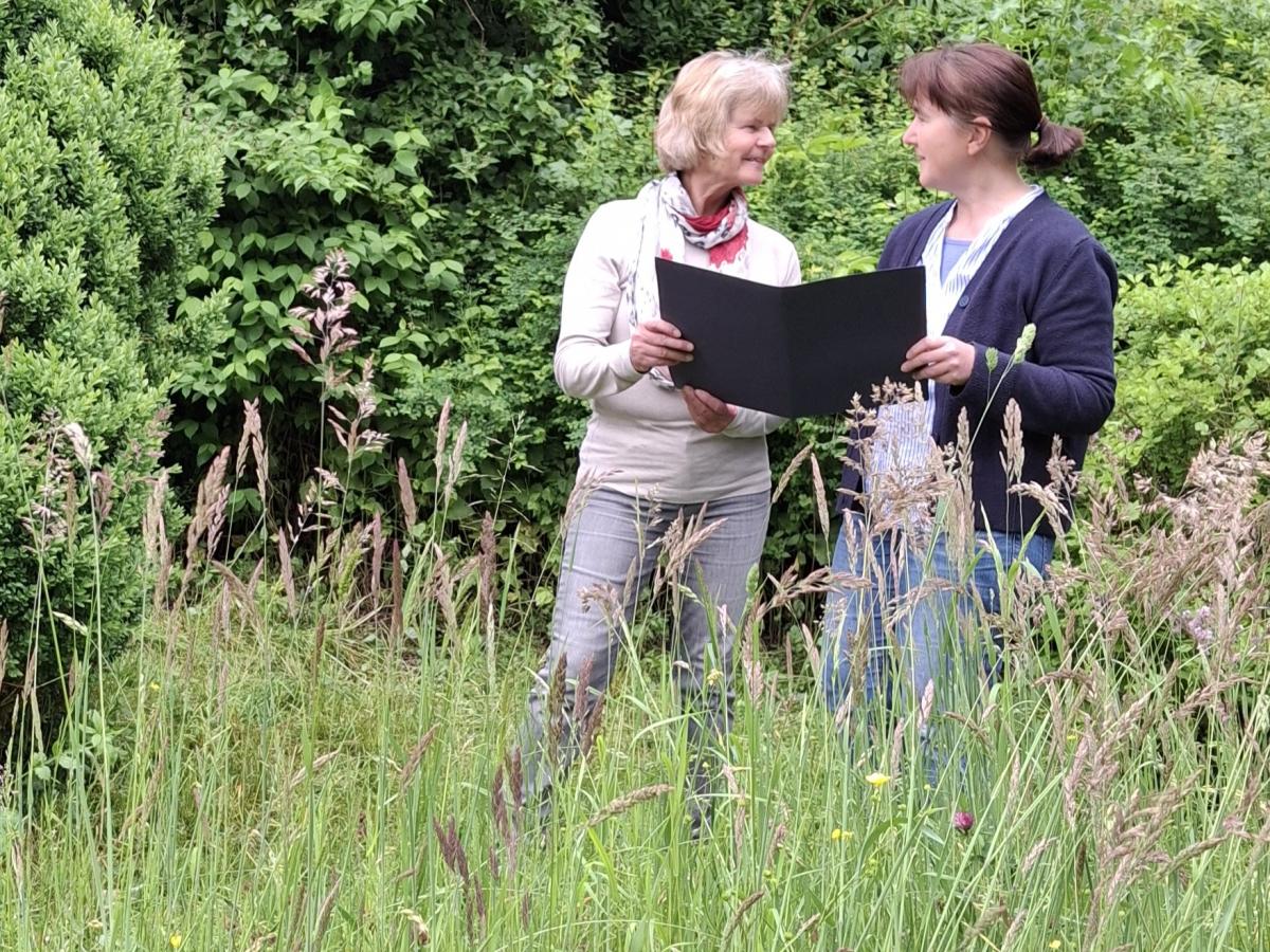 Zwei Frauen stehen in einer Wiese mit hohem Gras.