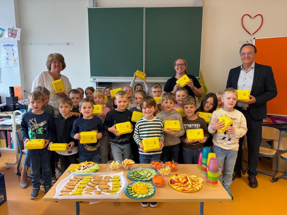 Kinder mit einer gelben Box in der Hand, im Hintergrund drei Erwachsene