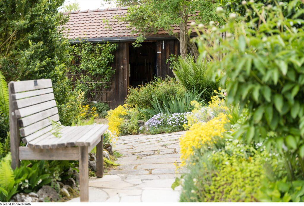 eine Bank steht in einem Garten, im Hintergrund sieht man einen Schuppen