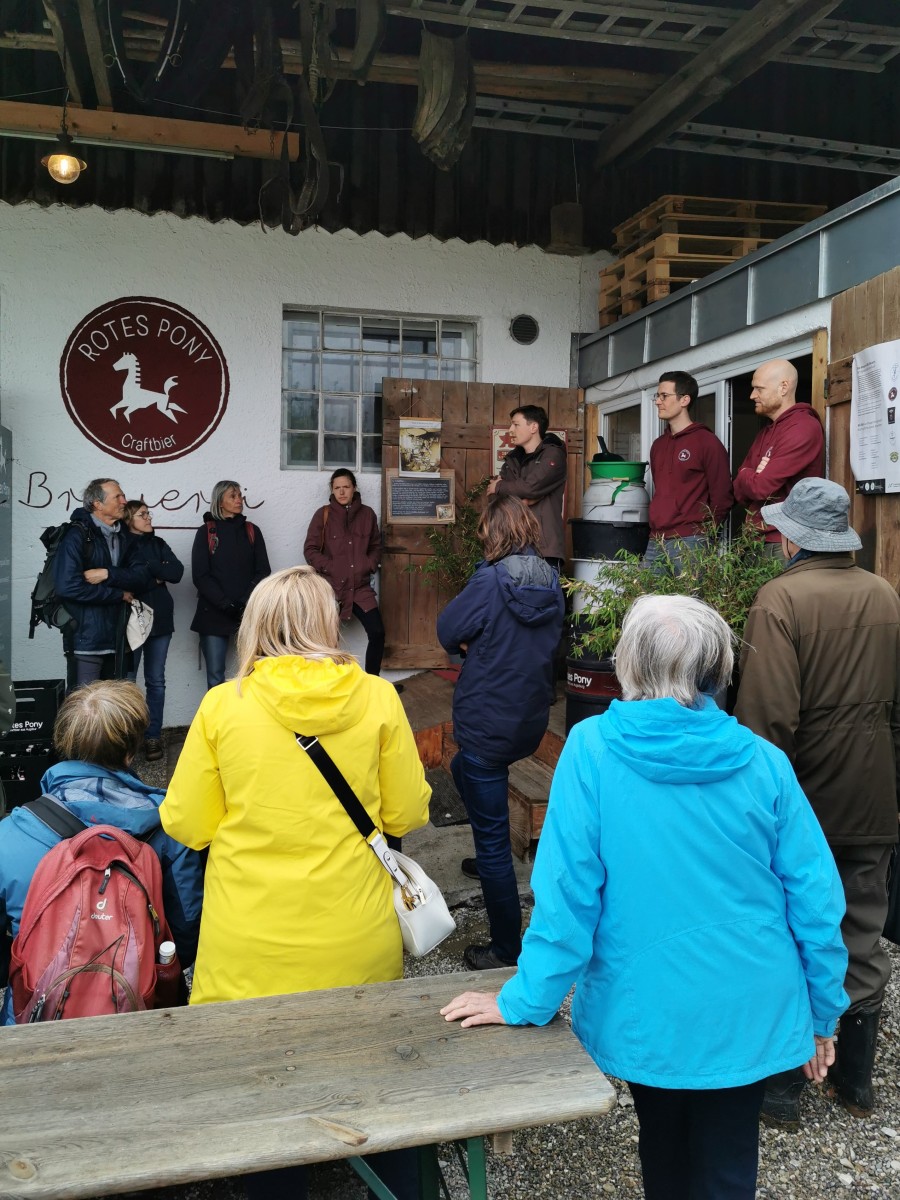 Das Foto zeigt eine Gruppe von Menschen, die vor einem Gebäude stehen und Ausführungen eines landwirtes zuhören.