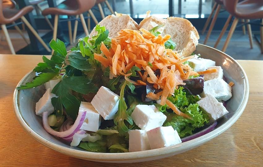 Salatschüssel mit Kopfsalat, Karotten, Schafskäse, Baguellescheiben auf einem Tisch im Restaurant