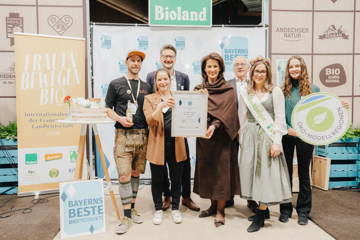 Sieben Personen, die vor dem Bioland Stand stehen, zwei Personen halten eine Urkunde und eine ein Schild mit dem Logo der Öko-Modellregionen