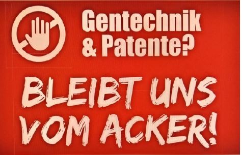 Rotes Plakat mit großer Aufschrift "Gentechnik & Patente? Bleibt uns vom Acker!" und einem Stoppschild