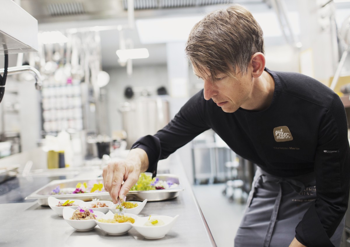 Küchenchef Christian Martin beim zaubern - gebeugt über eine Küchentheke streut er Grün zur Deko auf kleine weiße Schälchen mit selbstgemachten Aufstrichen