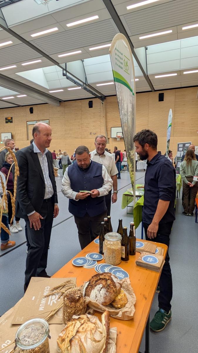Das Foto zeigt einen Mann an einem Infostand, der mehreren Personen etwas erklärt.
