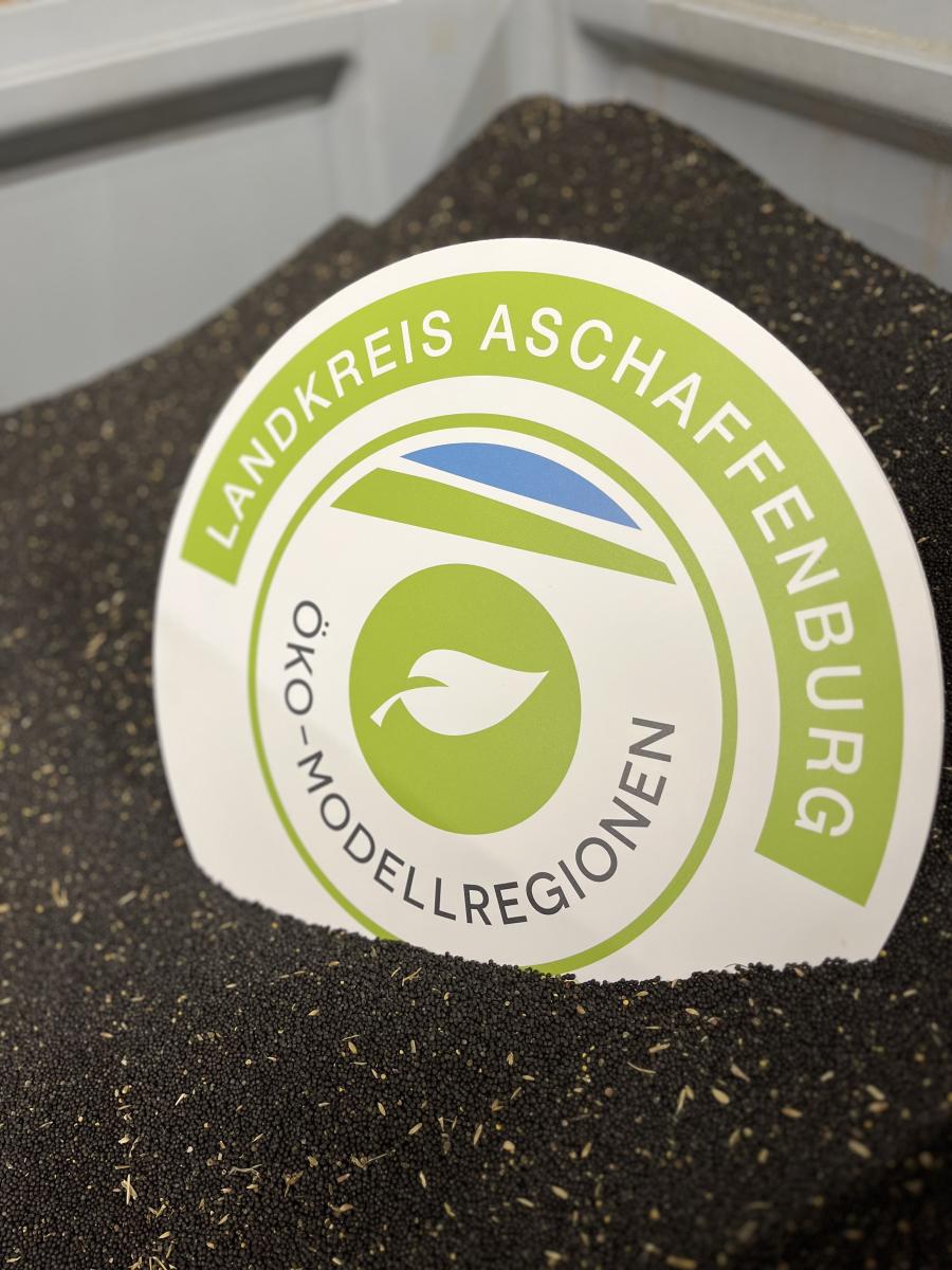 Schild mit dem Logo der Öko-Modellregion Landkreis Aschaffenburg in Rapskörnern