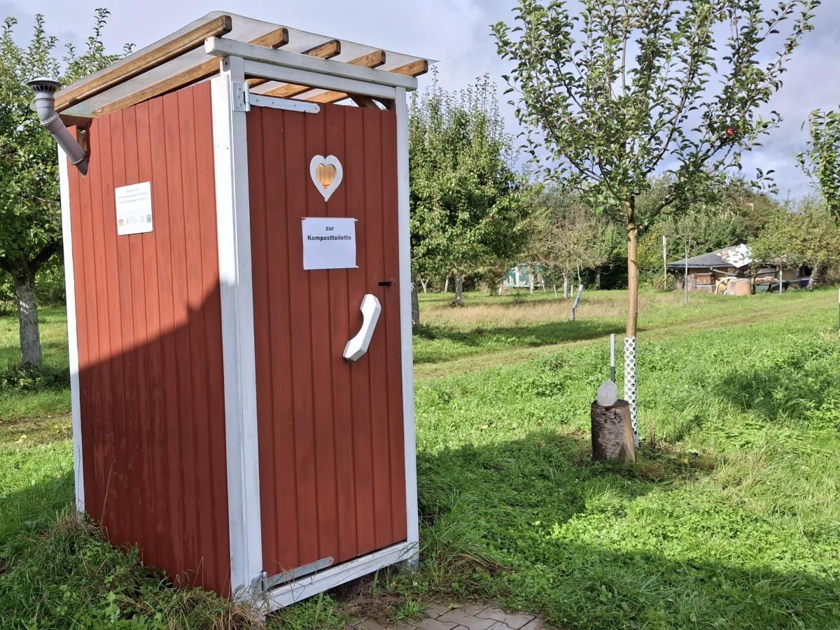 Kloo-Häuschen auf der Wiese, daneben ist ein kleiner Baum