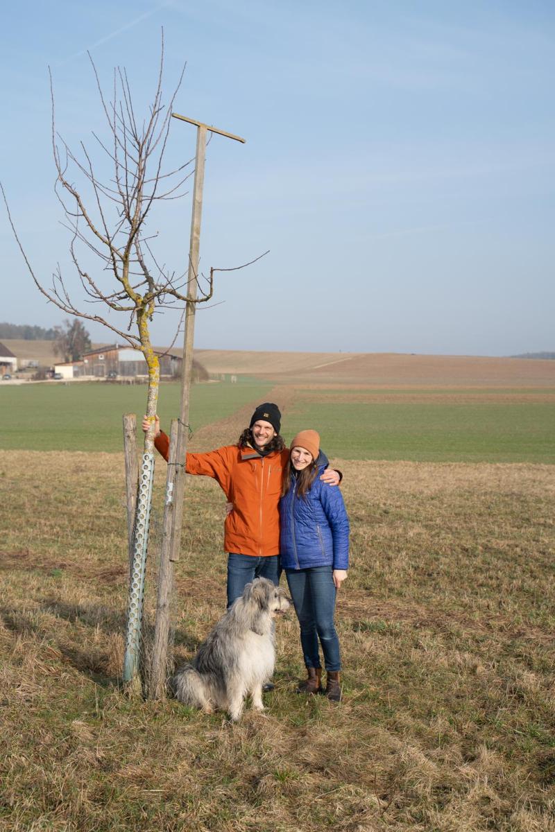 Steffi und Peter Riegg mit Hund Paco an einem Baum, an dem Kräuter und Stauden gepflanzt werden sollen