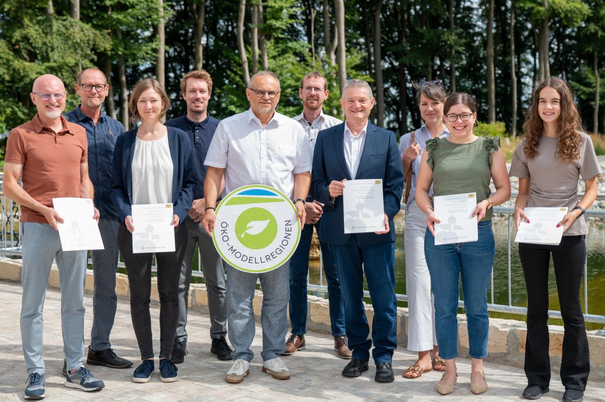 Gruppenfoto mit Öko-Modellregionsschild und fünf Förderbescheiden