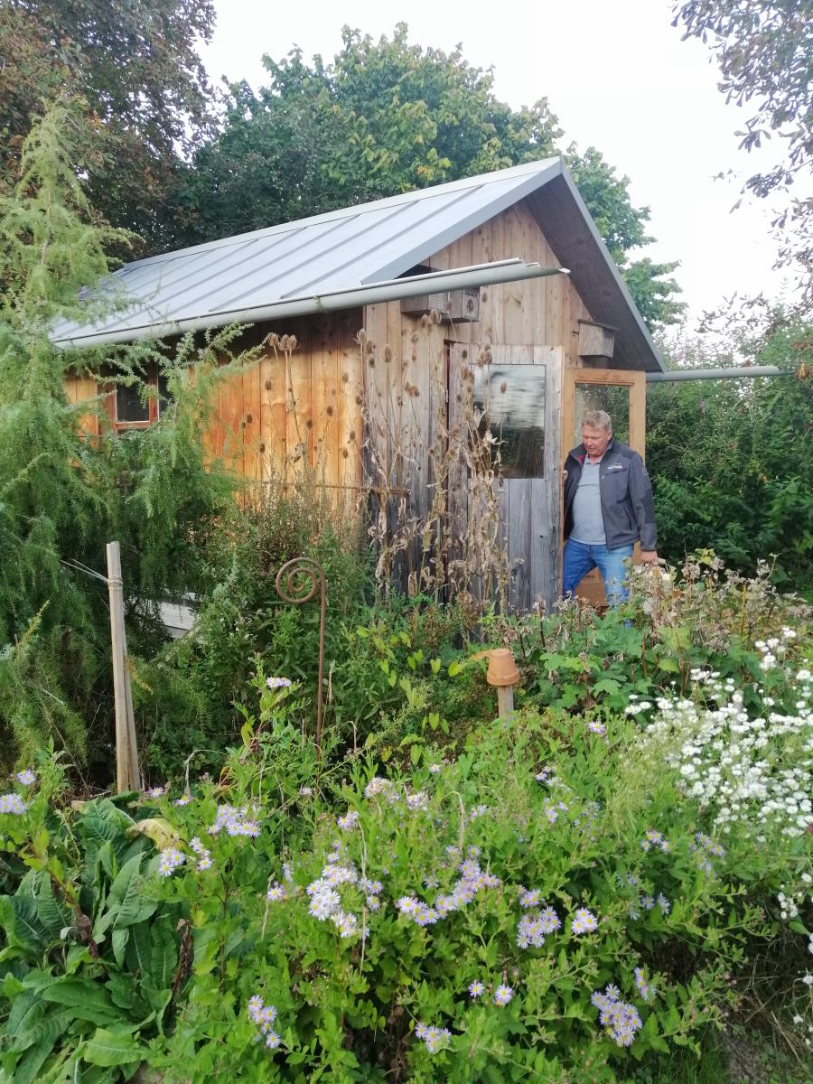 Mann vor Holzhütte und Gartenbeet